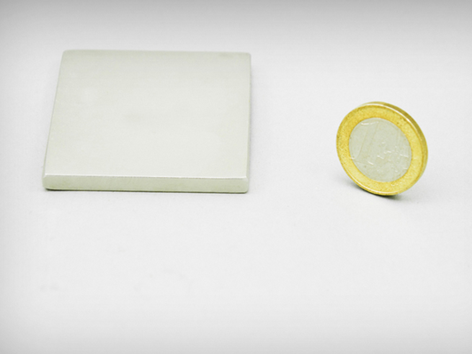 Een witte rechthoekige keramische tegel naast een goudgerande euro munt met blokmagneet 50x50x5 n45 magnetische kracht